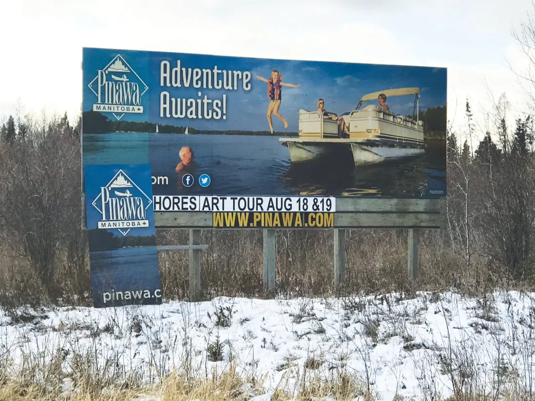 Travel Manitoba “Adventure Awaits” billboard for Pinawa beside a snowy road