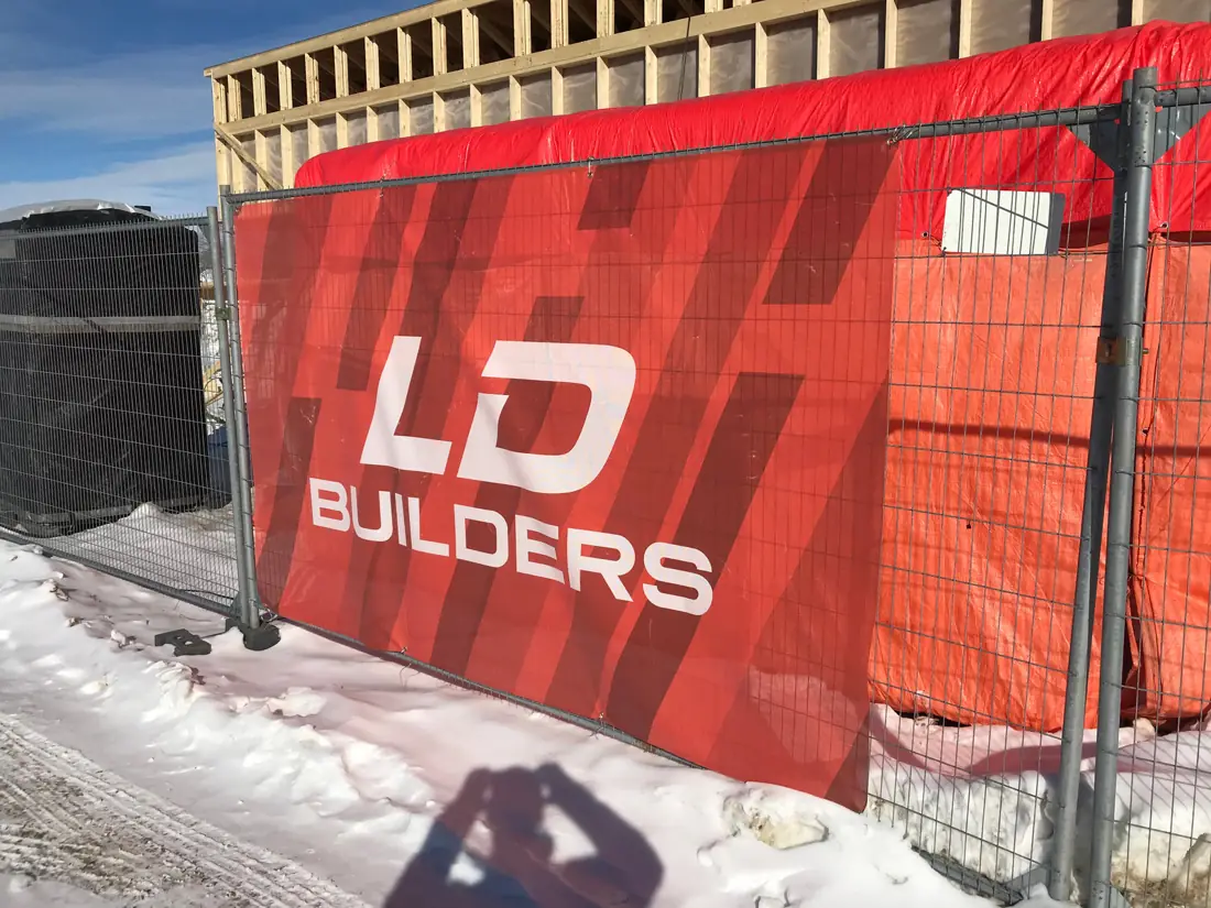 Red LD Builders fence-mesh banner on temporary fencing at a winter construction site